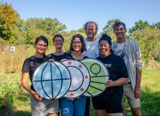 Das Foto zeigt das Team des WeltTellerFelds. Von links nach rechts sind zu sehen: Charlotte, Anna, Theresa, Nikolai, Mara und Lukas. Das Team steht am WeltTellerFeld und hält ein großes WeltTellerFeld Logo in den Händen.